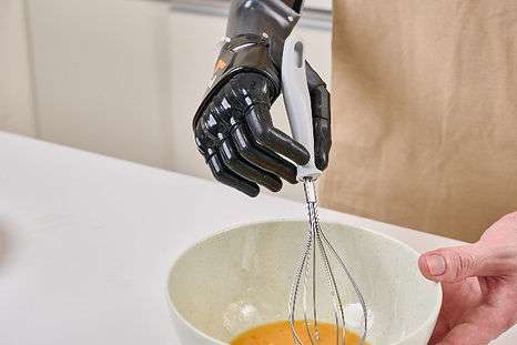 An upper limb young man is using his prothesis hand to hold a whisk to stir the egg in a bowl