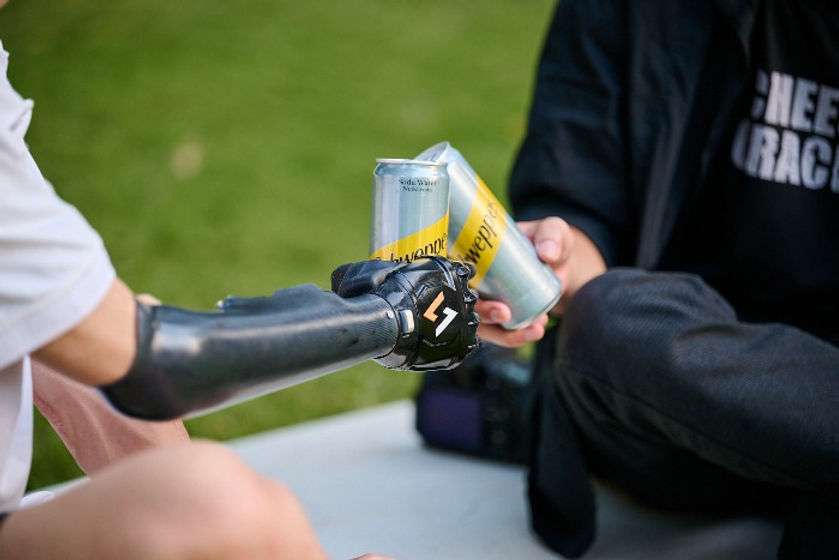 An upper limb young man wearing a white polo shirt is holding a can of beer with his prosthetic arm to cheer with his friend in a parkand to ride a bicycle in a part