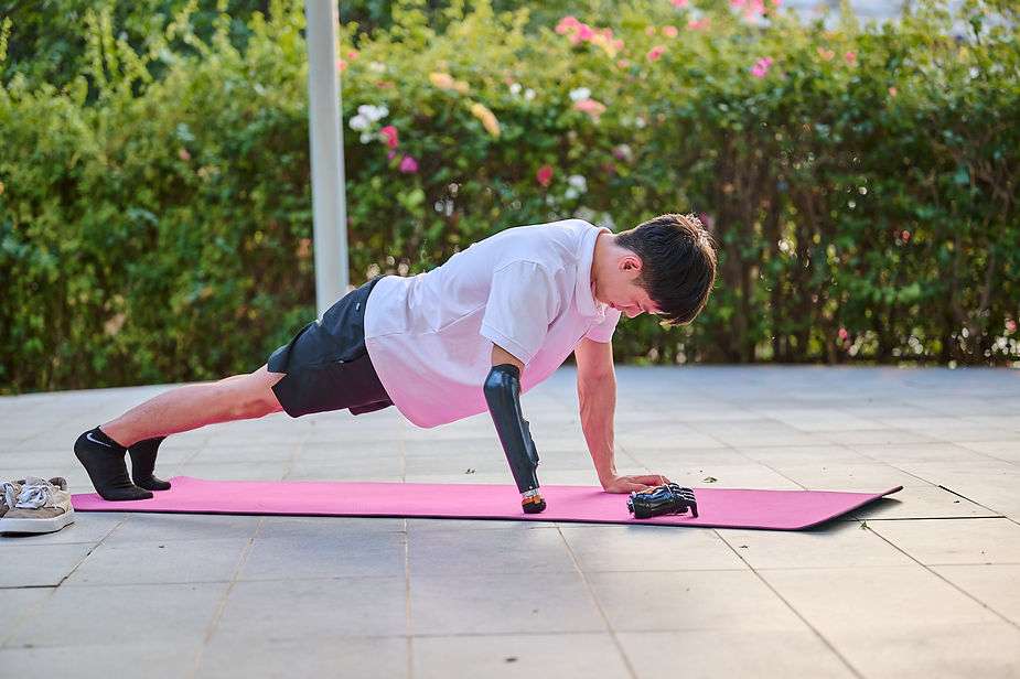 An upper limb young man is using his prothesis hand to do push up in a park