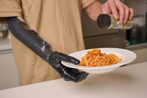 Person using a Vulcan prosthetic hand to spread jam on a slice of bread
