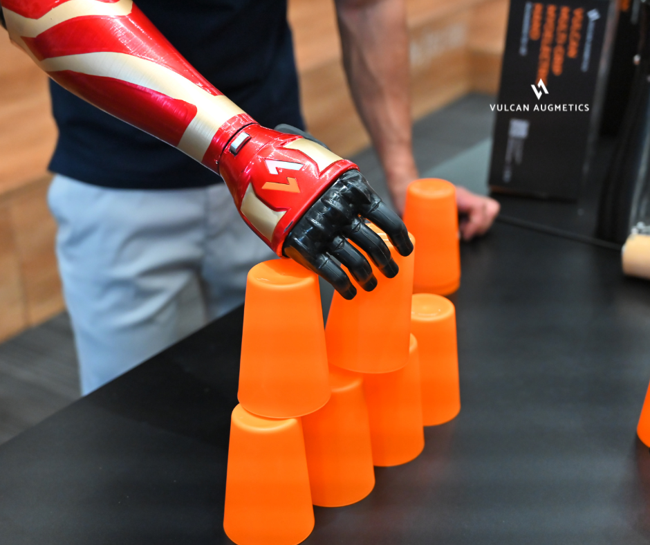 A male arm amputee wears a red prosthetic hand to hold an orange cup when playing cup stack